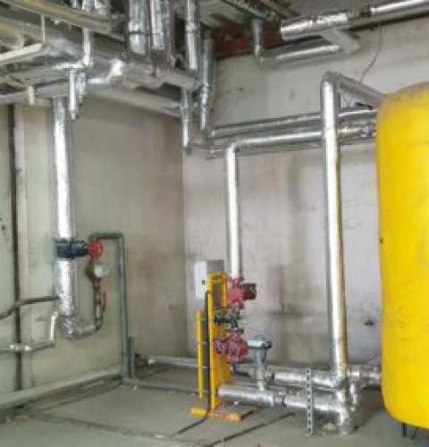 Système de chauffage industriel avec tuyaux isolés et une grande cuve jaune sous pression, situé dans une salle technique.
