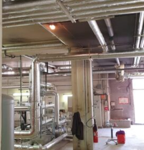 Vue d'une installation industrielle avec un réseau de tuyauterie isolé au plafond et au sol, dans une salle de maintenance technique.
